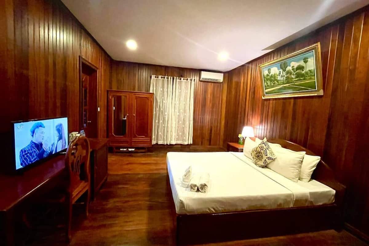 Une chambre d’hôtel avec des boiseries, un lit recouvert de draps blancs, un téléviseur posé sur une table en bois et une armoire.
