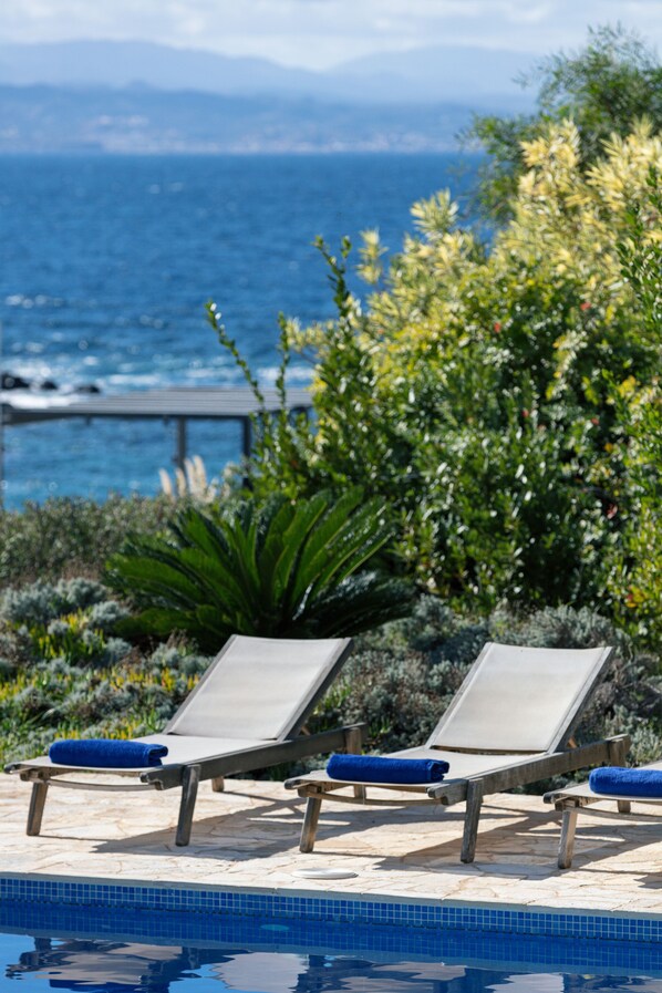 A poolside area with lounge chairs and a view of the ocean.