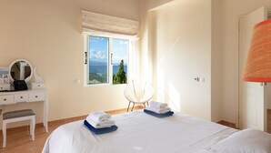 A bedroom with a bed, a desk with a mirror, a chair, and a window with a view of the sea. - Steps from the Beach, Sunset Views to Remember! (Chania)