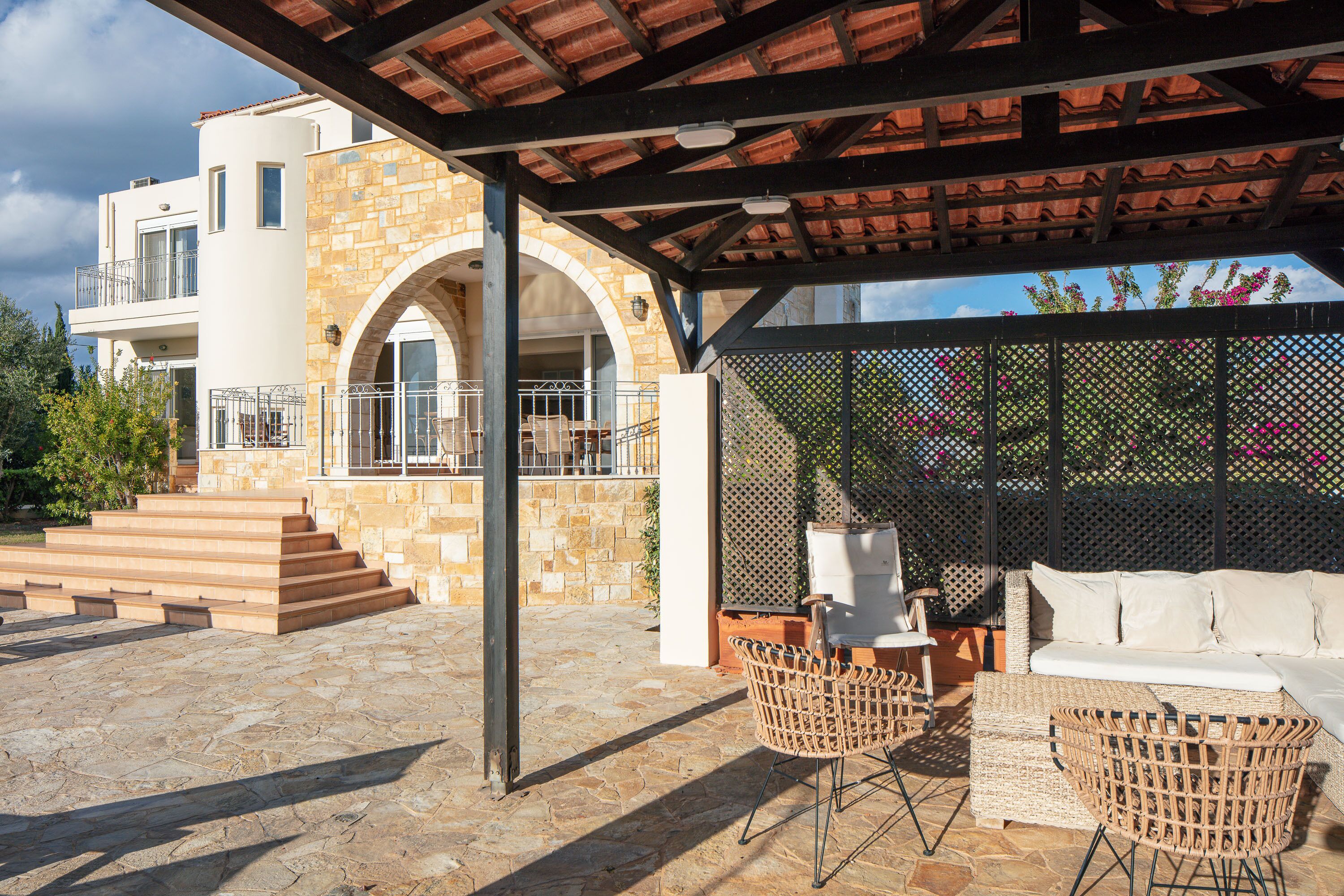A covered outdoor area with stone steps leading to a white building, wicker furniture, and a view of the sky.