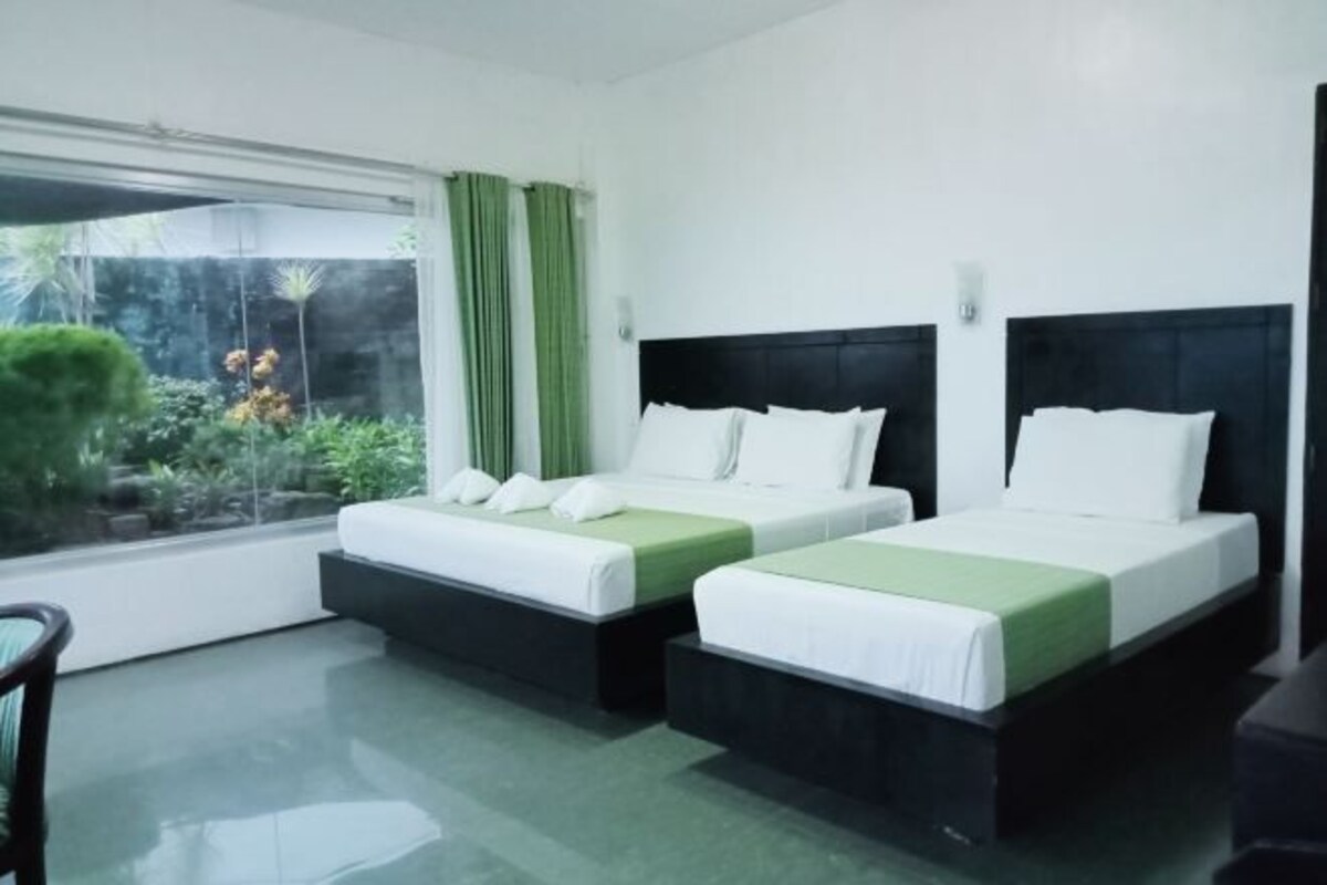 Een hotelkamer met twee bedden, een raam met gordijnen en uitzicht op groen.