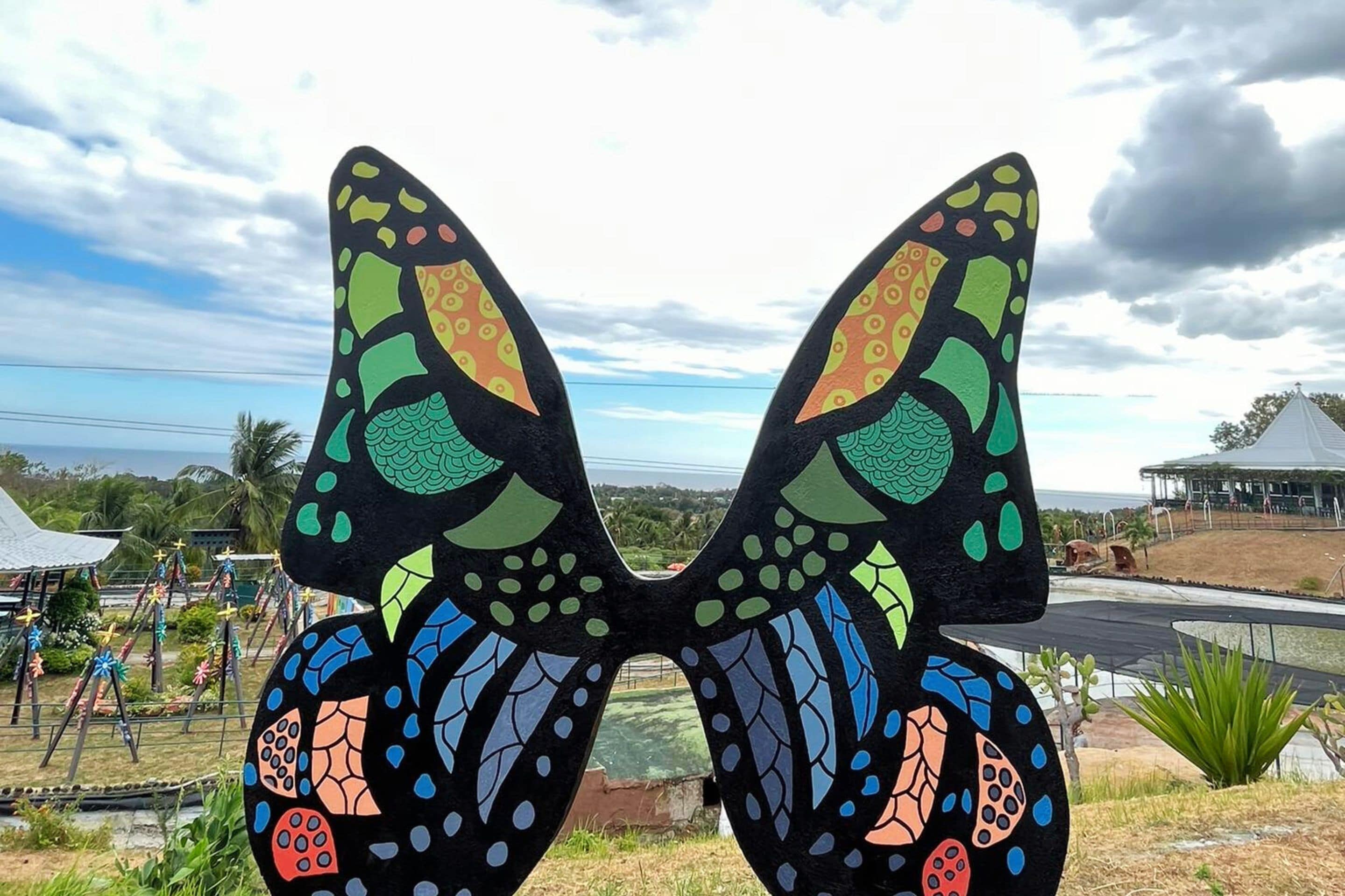 A colorful butterfly sculpture with a view of a park and a building in the background.