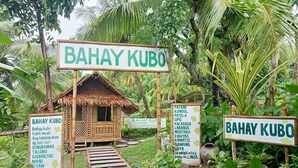 Een bordje voor 'Bahay Kubo' met een rieten dak en een tuinpad dat ernaartoe leidt.