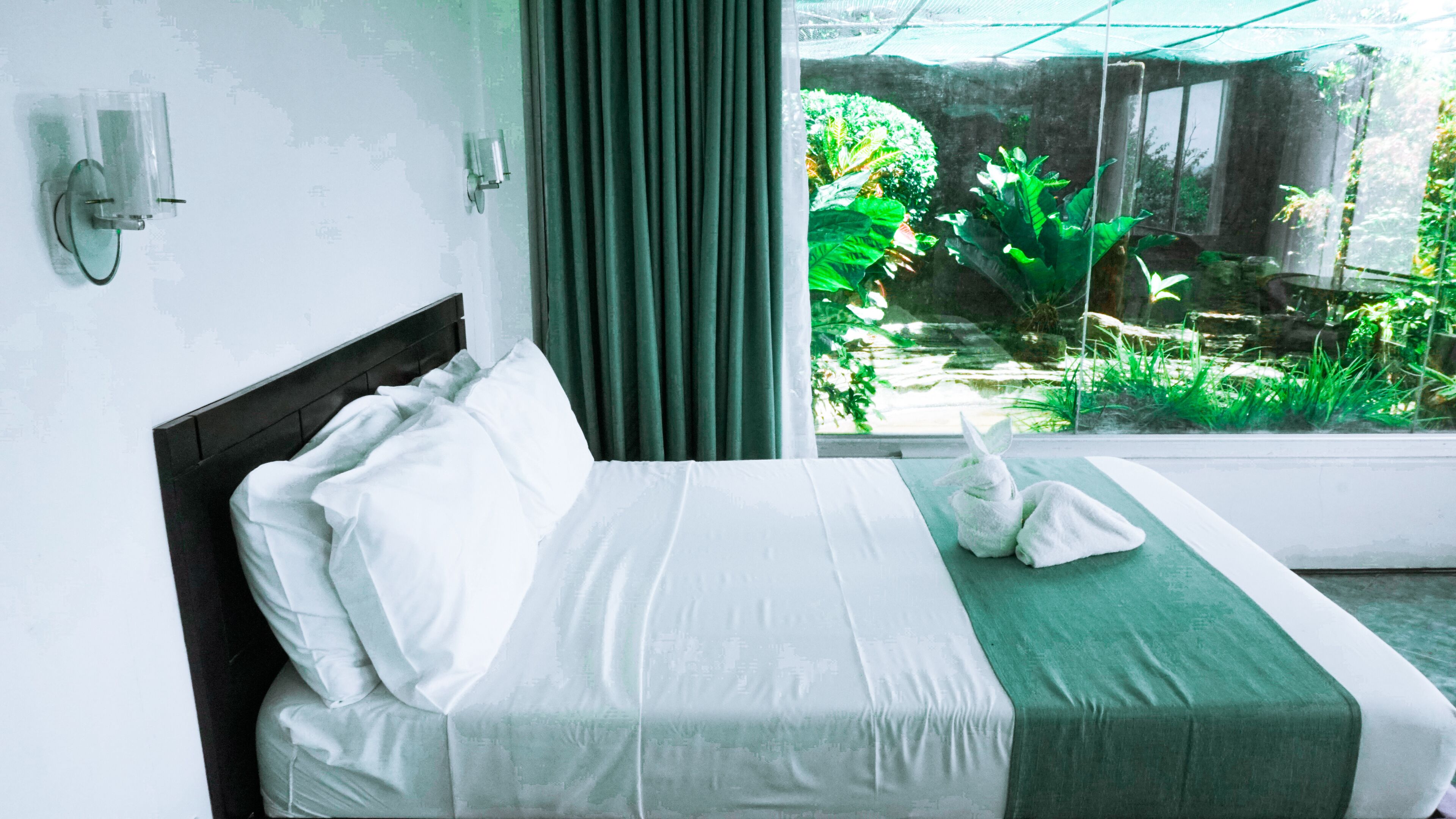 A bed with white linens, a green bedspread, and a towel shaped like a rabbit.
