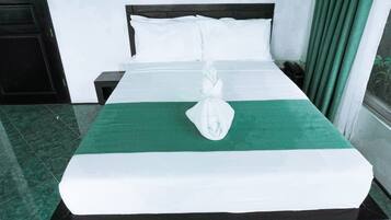 Un letto rifatto con lenzuola bianche e un tocco di verde, un comodino con un telefono e una finestra con tende.