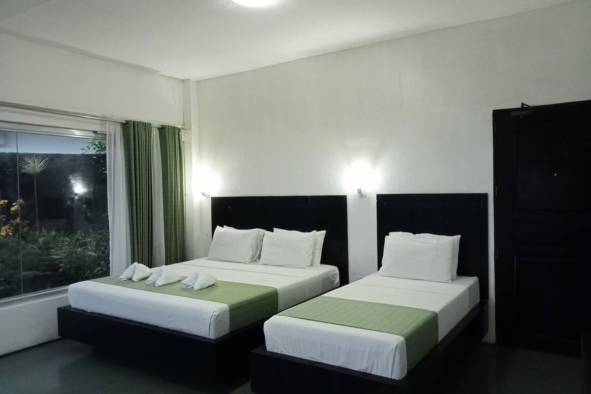 Habitación de hotel con dos camas individuales, un ventanal con cortinas y un armario oscuro.