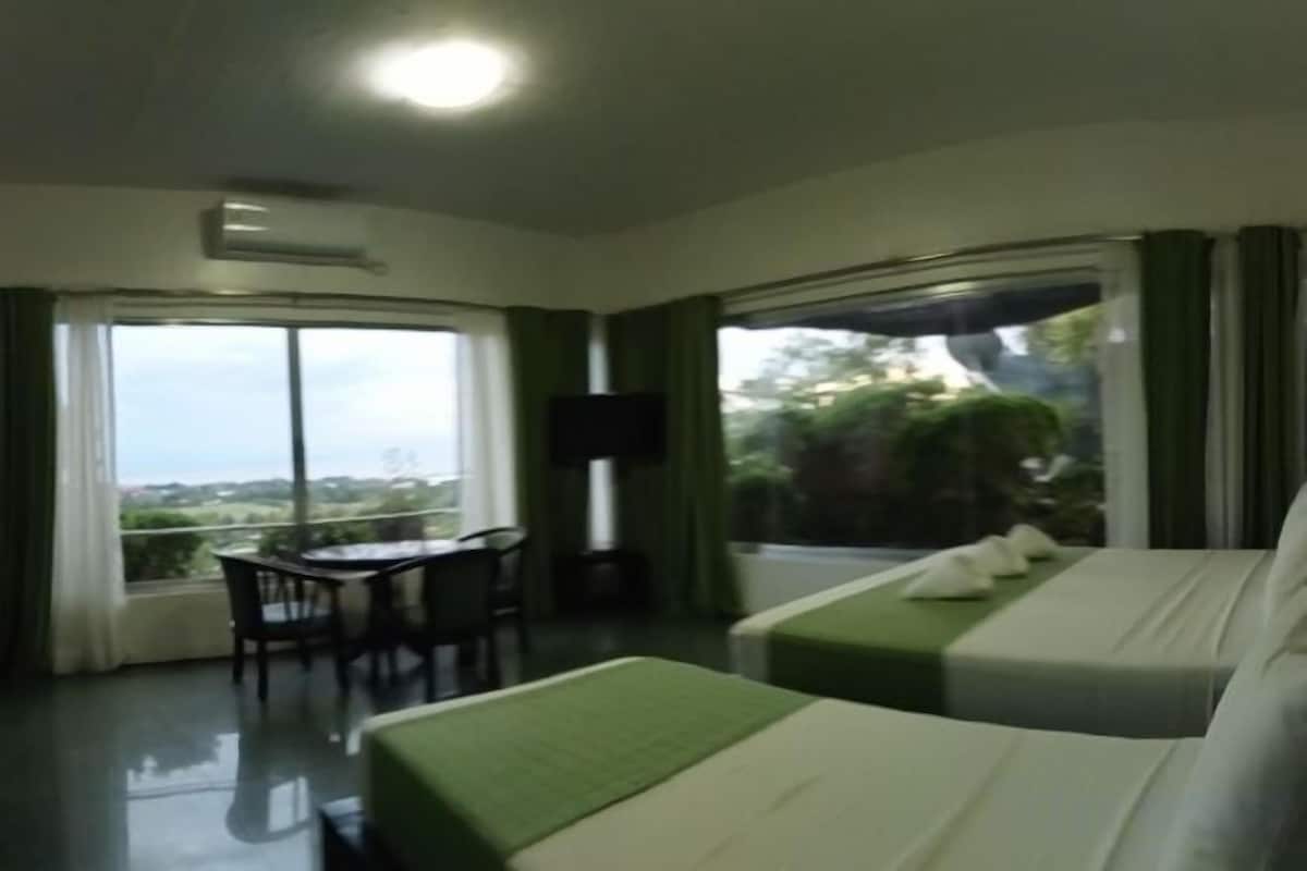 Habitación de hotel con una cama, una mesa y una silla. Un ventanal grande ofrece vistas al exterior.