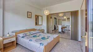 A bedroom with a bed, bedside table, and a mirror. There is a dining area with a table and chairs visible through an open door. - Apartment 1899/23271 (Istria - Rovinj), 1000m from the beach (Rovinj)