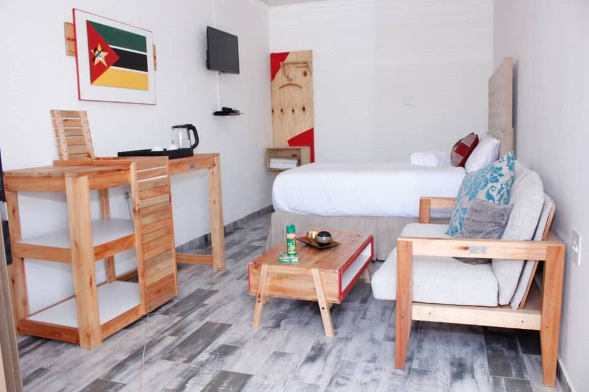 A small, modern room with a bed, a wooden desk, a chair, and a sofa.