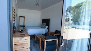 A bedroom with a bed, a wooden dresser, a small table, and a chair. - Lawu Le Ngwenya Guest House (Motshane)