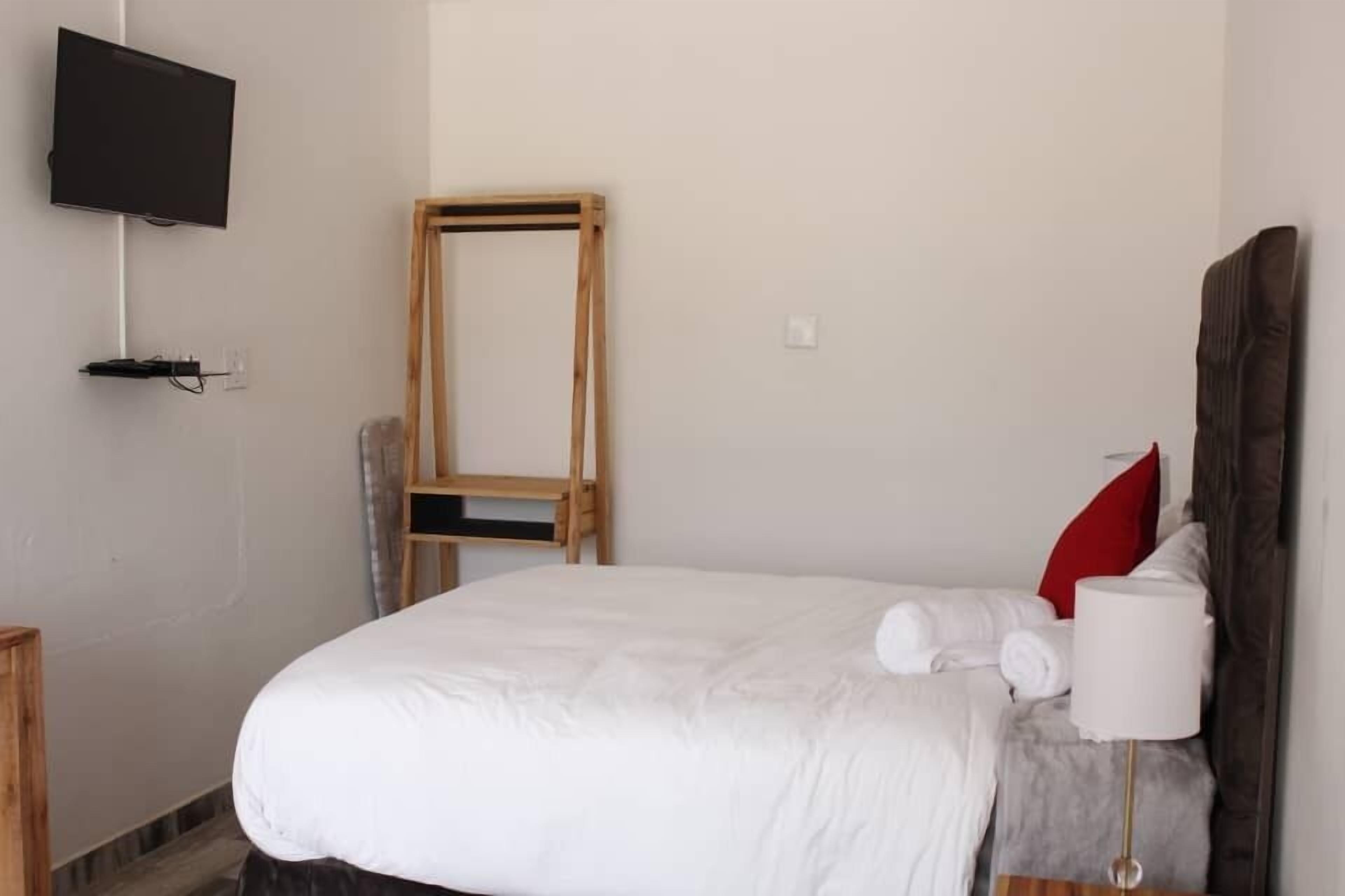 A neatly made bed with white bedding, a wooden headboard, and a red pillow. A flat-screen TV is mounted on the wall above the bed.