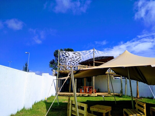 A covered outdoor area with a white wall, a wooden table, and a canopy structure.