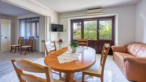 A dining area with a wooden table and chairs, a TV mounted on the wall, and a view of greenery through a window. - Apartment 1899/23273 (Istria - Rovinj), 1000m from the beach (Rovinj)