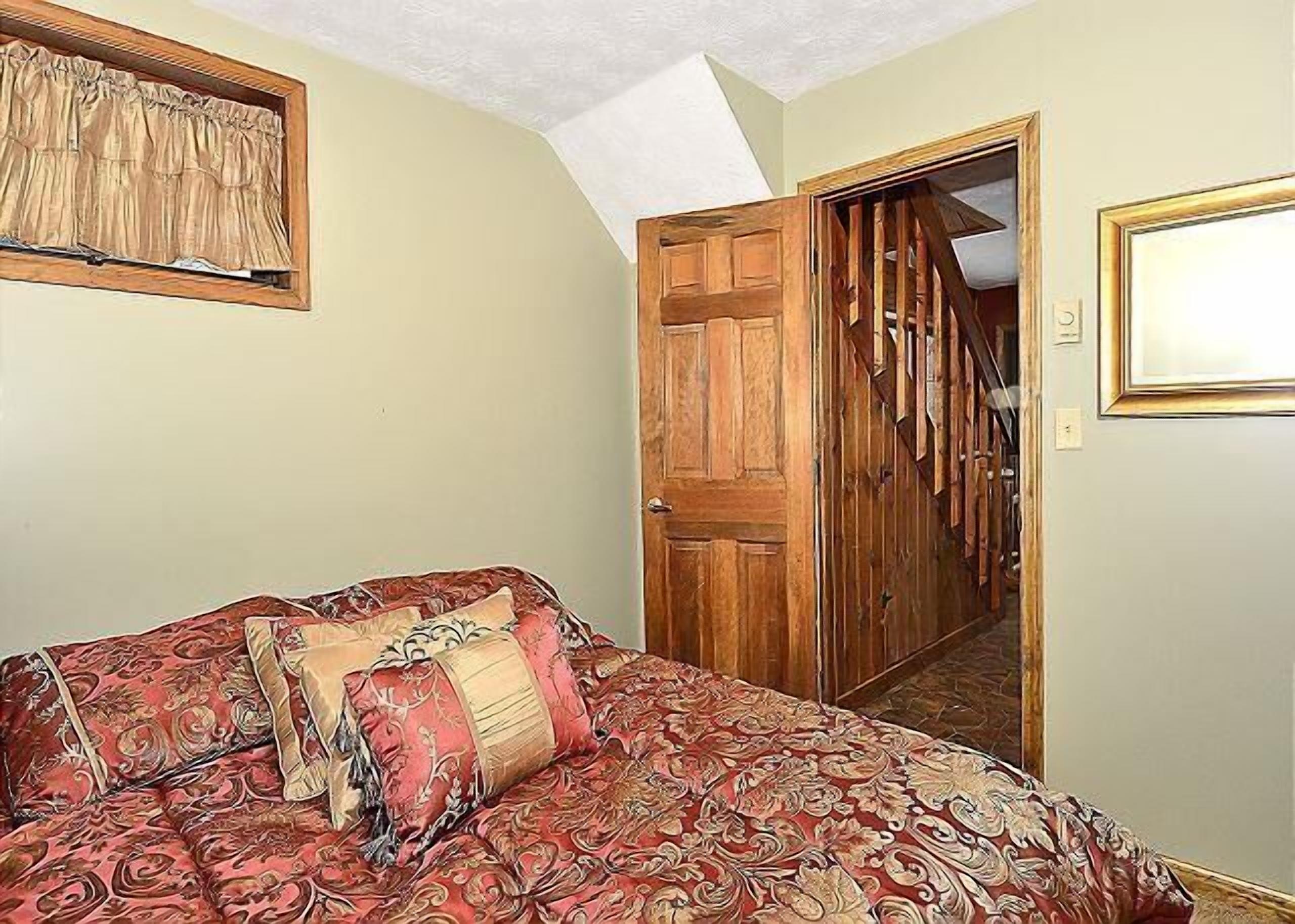 A bedroom with a bed, a wooden door, and a window with curtains.