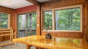 A wooden cabin interior with a large dining table and benches, large windows with forest views, and a red accent wall. - NF17- Cool, Creekside Home! Hot Tub! Pets ok! (Davis)