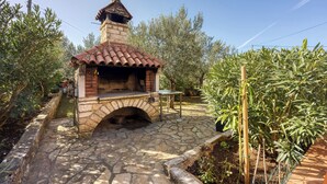 A stone-built outdoor oven with a tiled roof, surrounded by olive trees and a stone pathway. - Apartment 1899/23274 (Istria - Rovinj), 1000m from the beach (Rovinj)