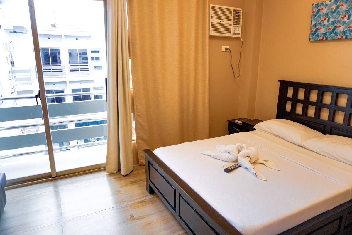 Une chambre d’hôtel avec un lit, une fenêtre avec des rideaux, un climatiseur fixé au mur et un tableau.