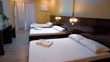 A hotel room with two beds, a desk, a chair, a plant, and a bathroom with a shower curtain.