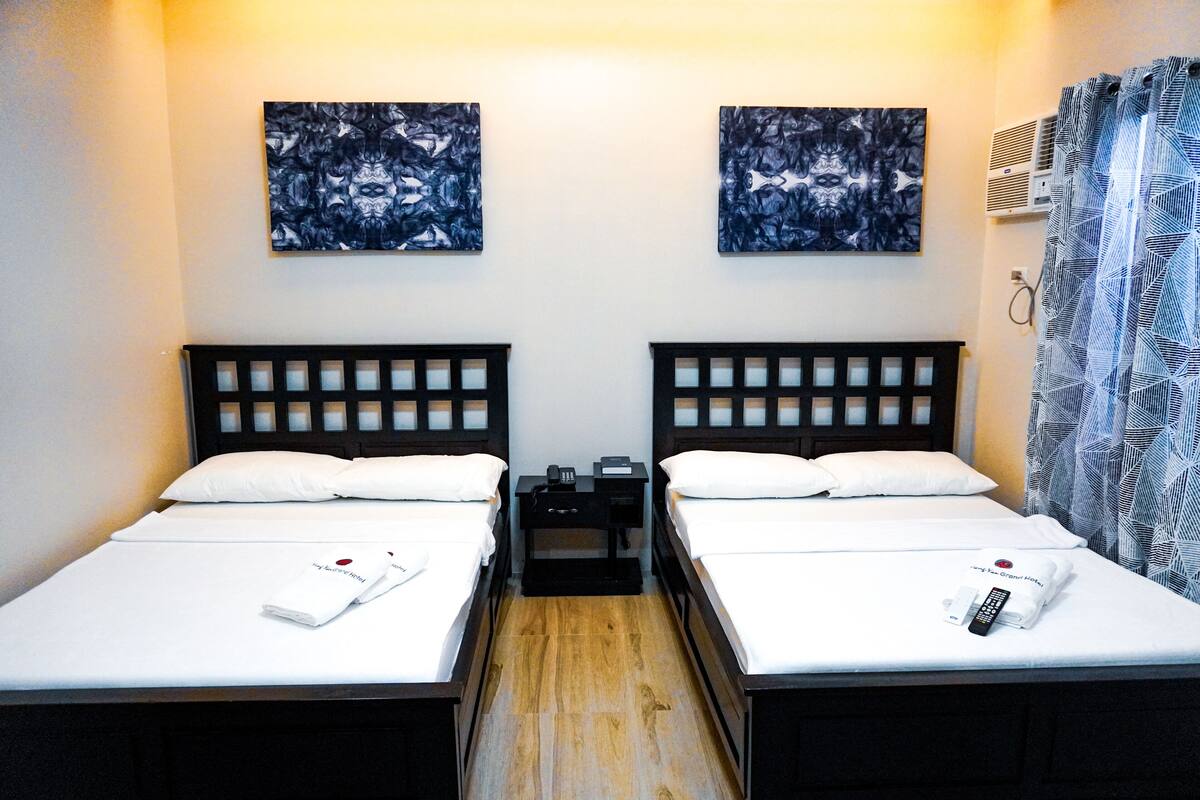 Une chambre d’hôtel avec deux lits simples, un plancher en bois, une table de chevet entre les lits et des œuvres d’art accrochées aux murs.