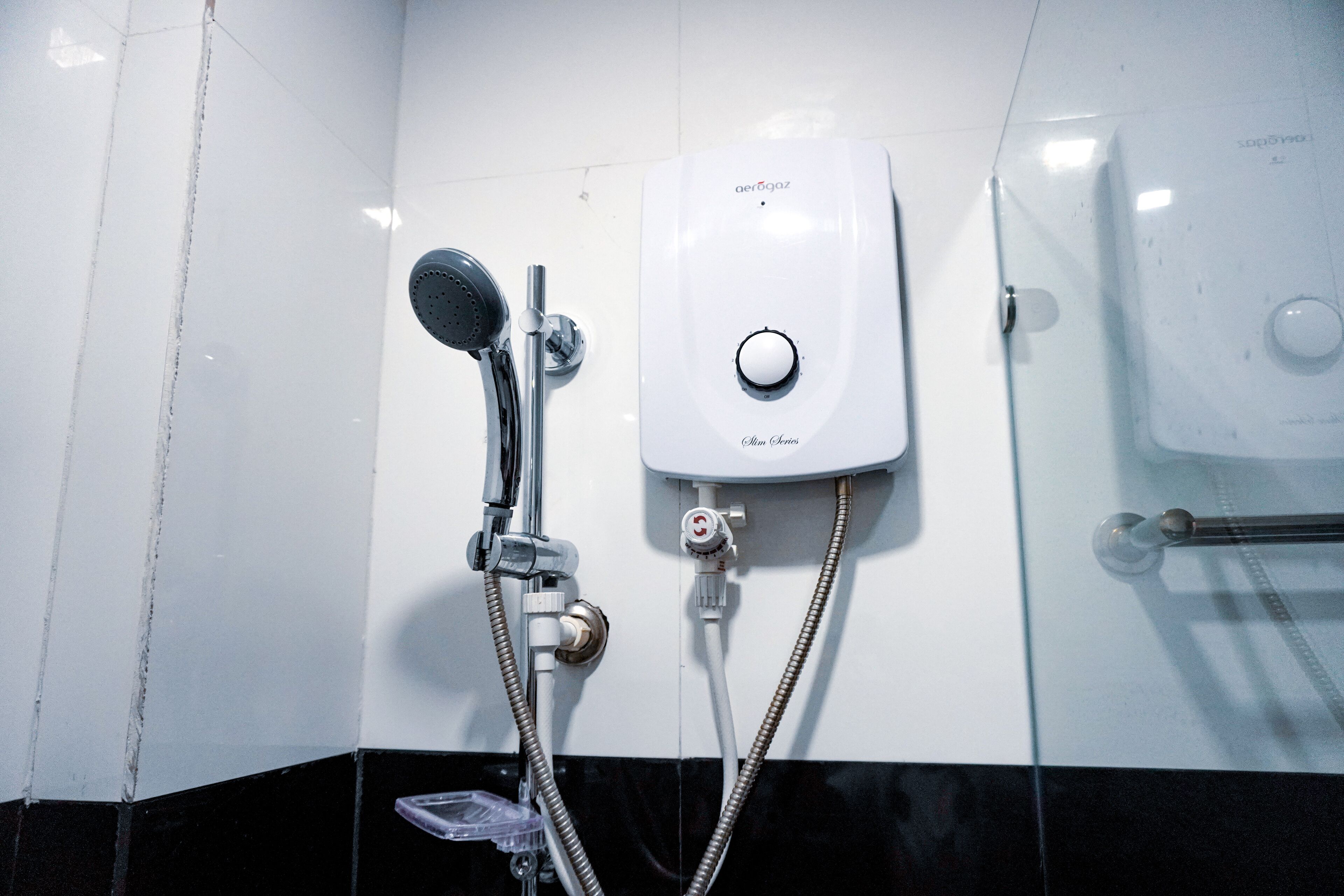 A modern bathroom with a wall-mounted shower, a soap dispenser, and a hand dryer.
