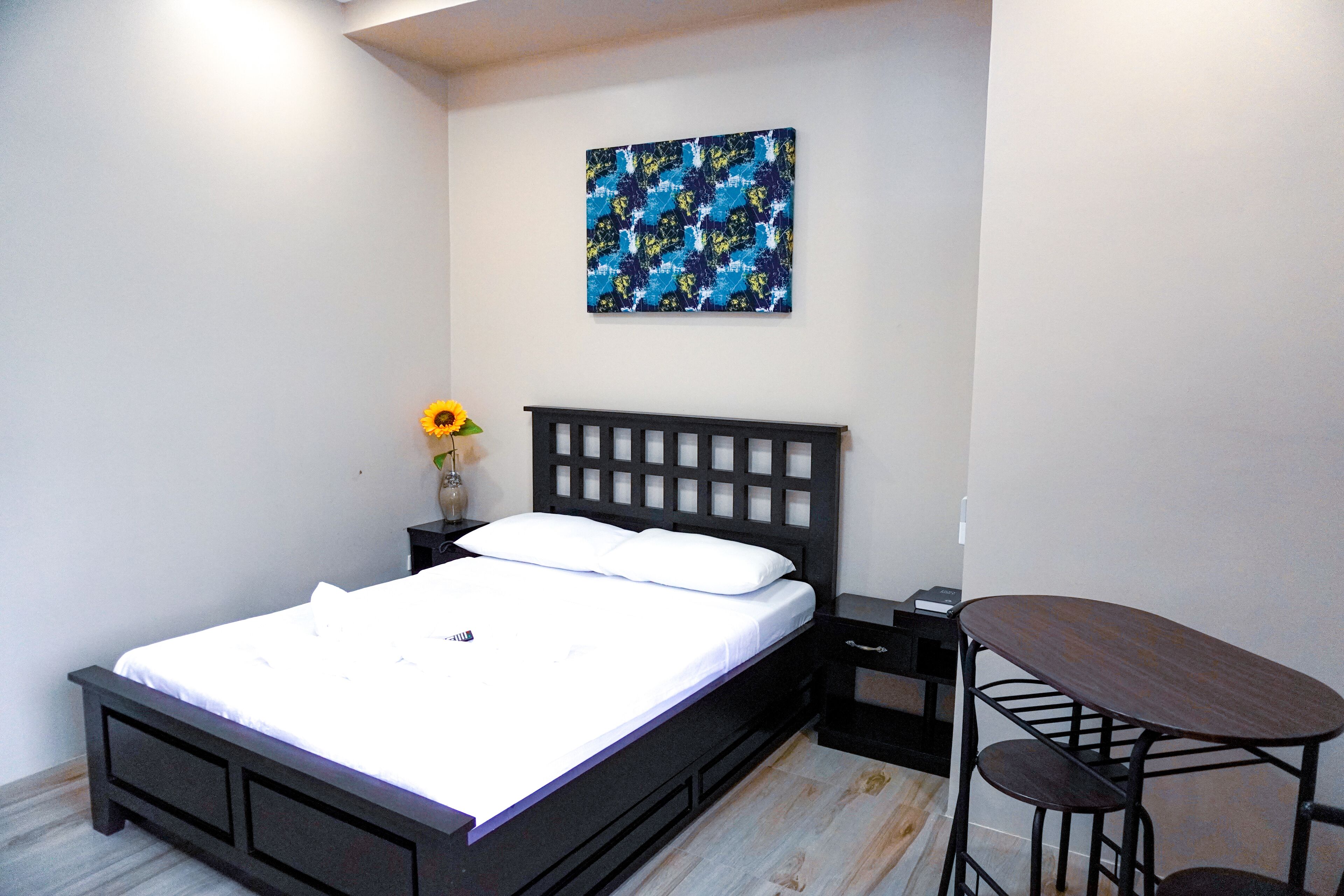 Quarto com cama, mesa de cabeceira, mesa e um quadro na parede.