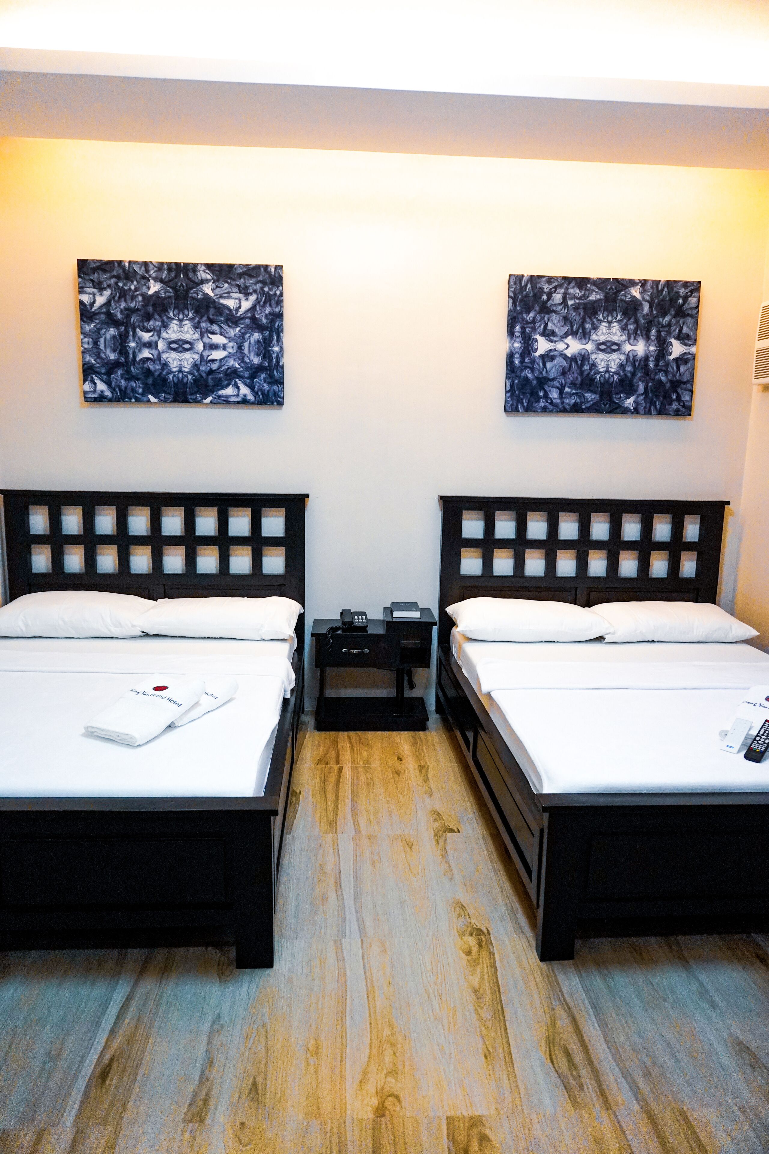 A hotel room with two beds, wooden flooring, and artwork on the walls.