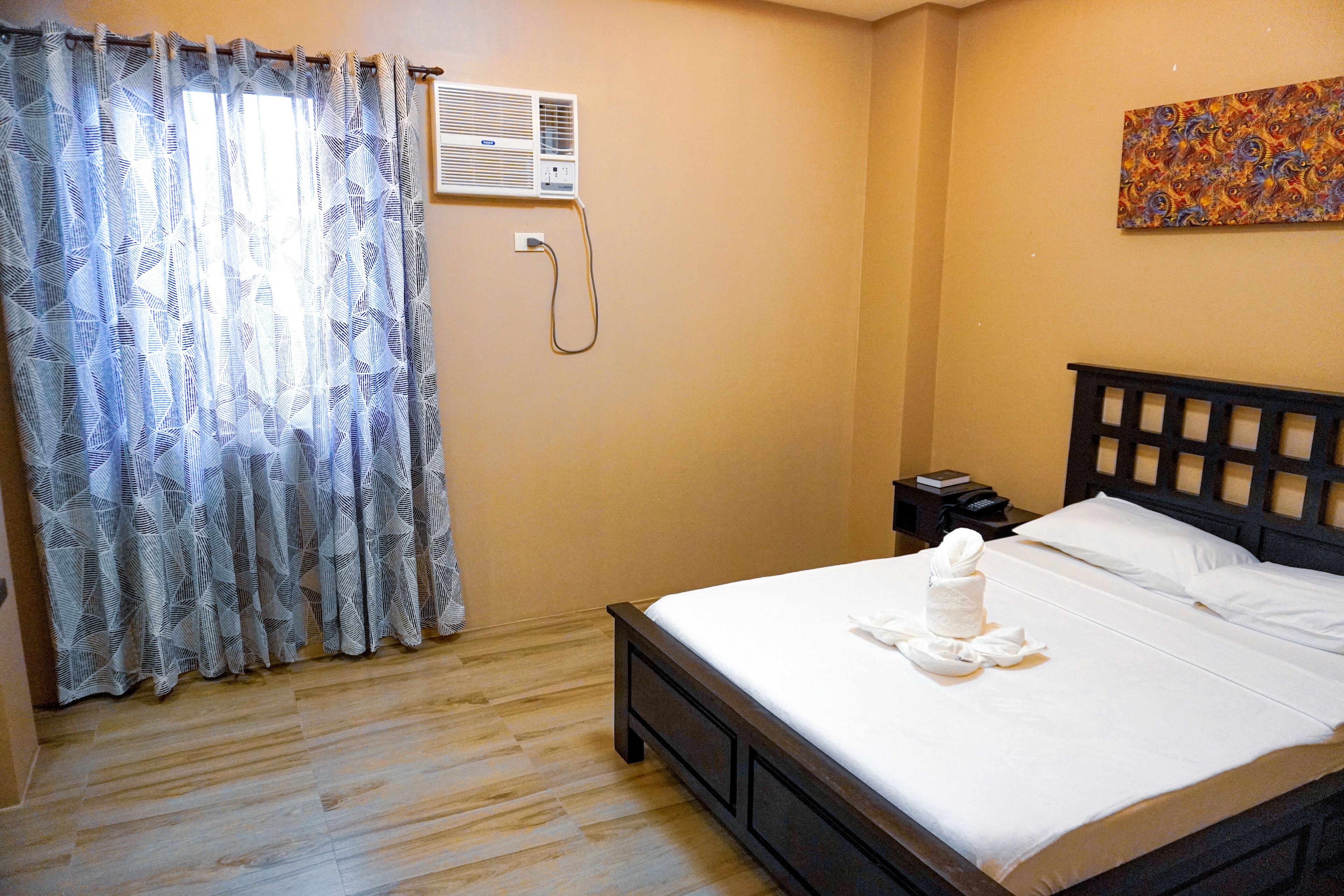 Habitación de hotel con cama, mesita de noche, aire acondicionado y ventana con cortinas estampadas.