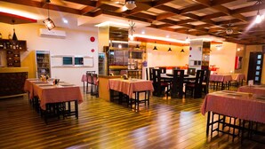 A restaurant with wooden flooring, tables with pink tablecloths, and hanging pendant lights.