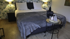 A neatly made bed with a grey blanket, two bedside lamps, and a small table with a water bottle and a welcome sign. - B & B Aphrodite (Zonnebeke)