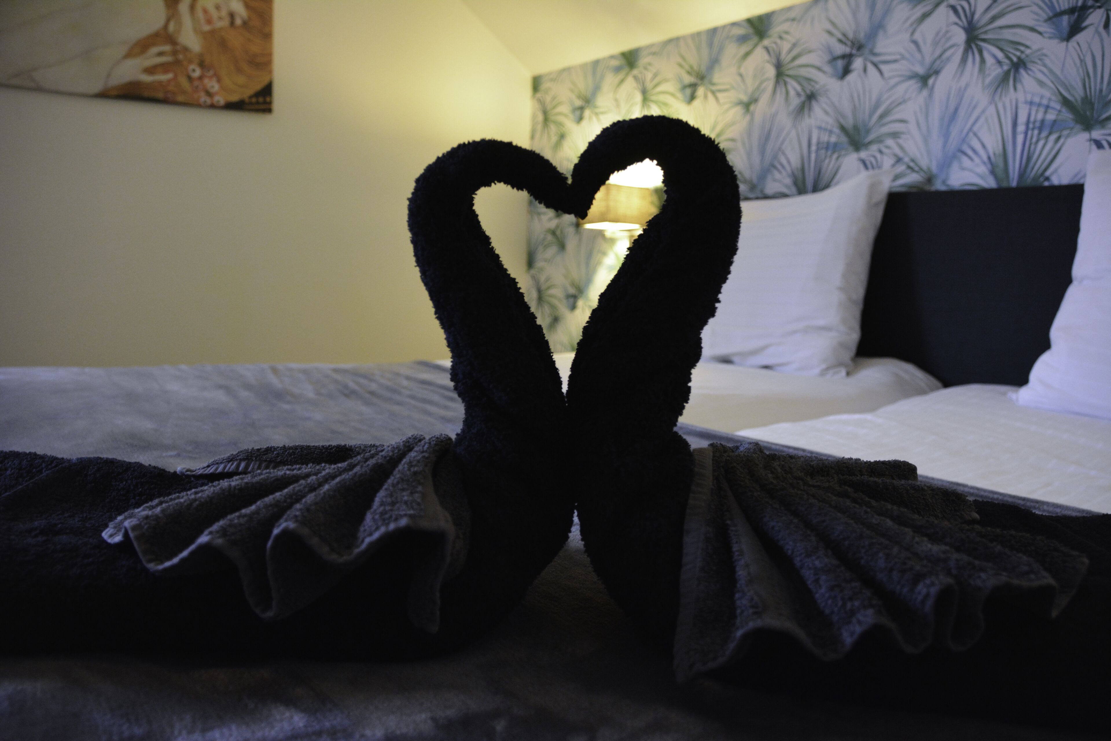 Una cama con una toalla dispuesta en forma de corazón y un cabecero estampado.