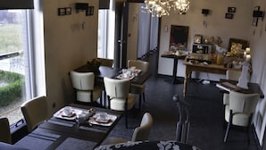 A dining area with a long table set for four, surrounded by chairs. There is a chandelier above the table, and the room has a modern design with a dark floor and light walls. - B & B Aphrodite (Zonnebeke)