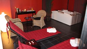 A spa room with a red carpet, two wicker chairs, a massage table, a small table with candles, and a white reception desk. - B & B Aphrodite (Zonnebeke)