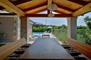 A covered outdoor seating area with a pool in the background.