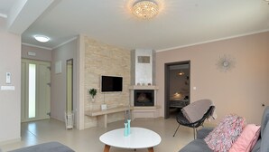 A living room with a stone fireplace, a flat-screen TV, a round coffee table, and a grey sofa with a pink pillow. - Villa 1924/23637 (Istria - Poreč), 3500m from the beach (Poreč)