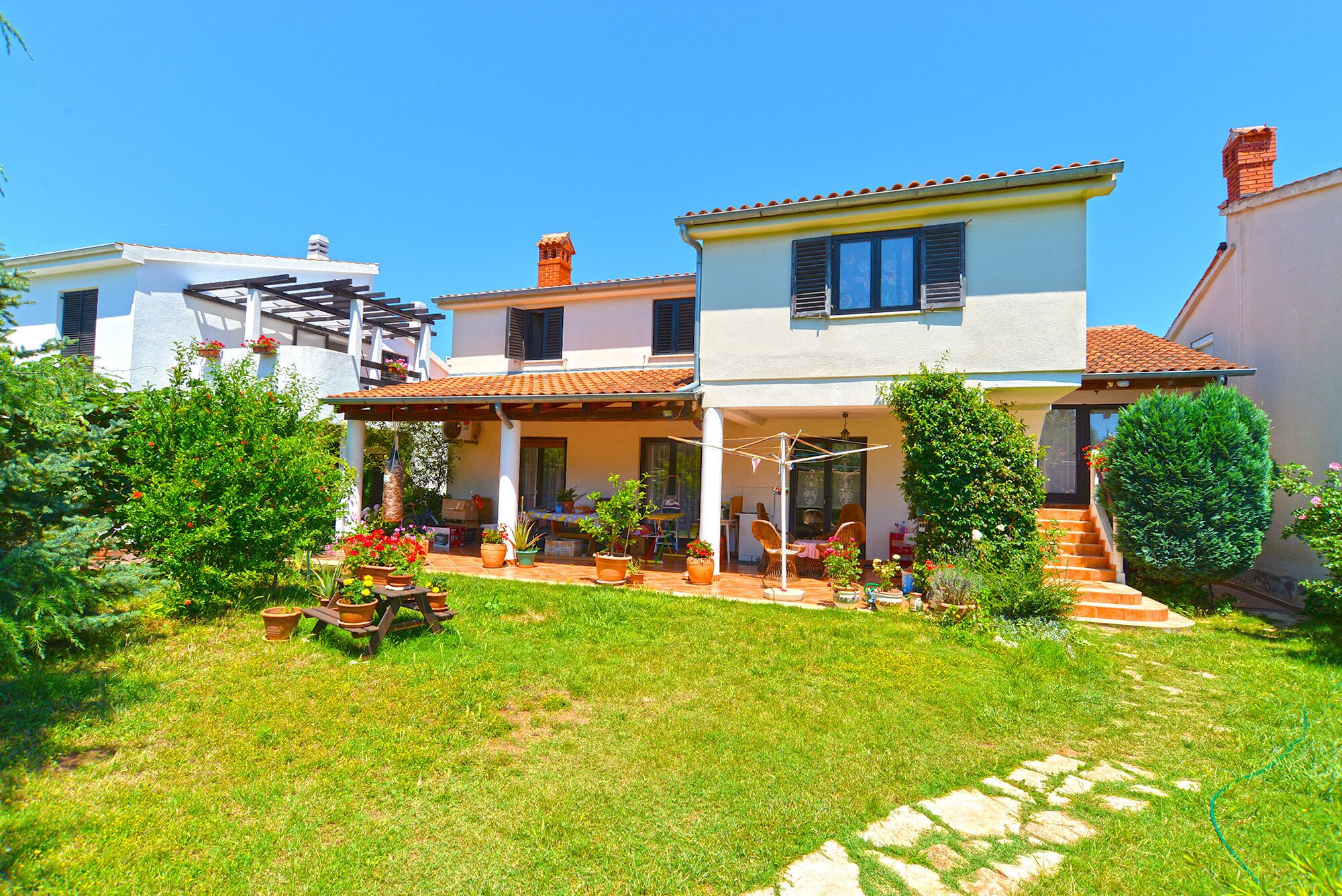 A two-story house with a covered patio, a garden with potted plants, and a staircase leading to the upper floor.