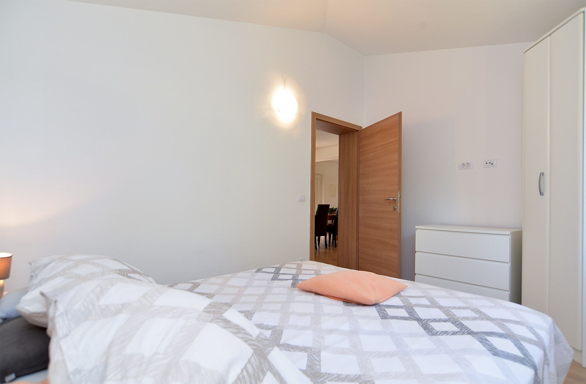 A bedroom with a bed, a nightstand, a dresser, and a wooden door.