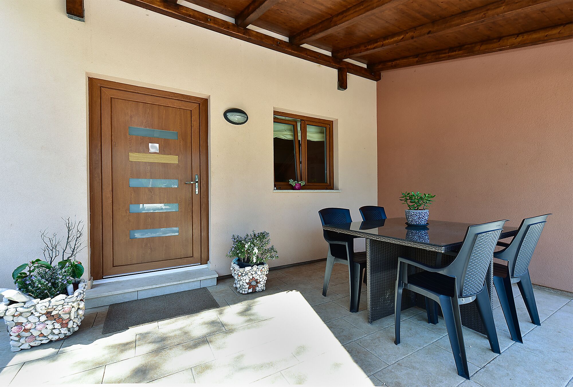 A patio area with a wooden door, a window, a table with chairs, and potted plants.