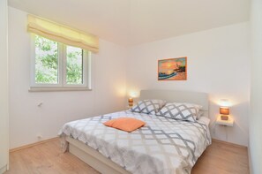 Una camera da letto con un letto, una finestra vista alberi, un quadro al muro e due abat-jour.