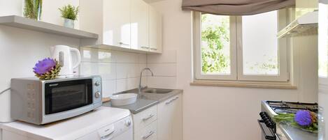 A compact kitchen with white cabinets, a microwave, a sink, and a stove.
