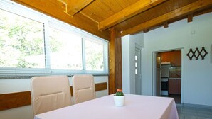 Un coin repas avec une table dressée pour quatre personnes, un petit cactus posé sur la table et une cuisine visible à travers une porte ouverte.