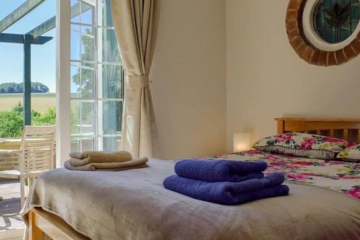 A bedroom with a bed, a window, a view of the outdoors, and a wooden bench outside.