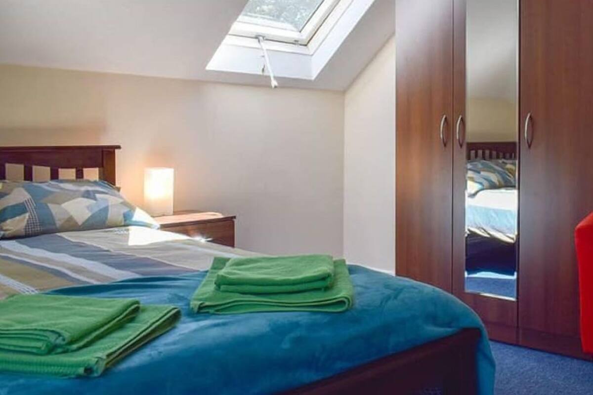 A bedroom with a bed, a nightstand, a wardrobe, a red chair, and a skylight.