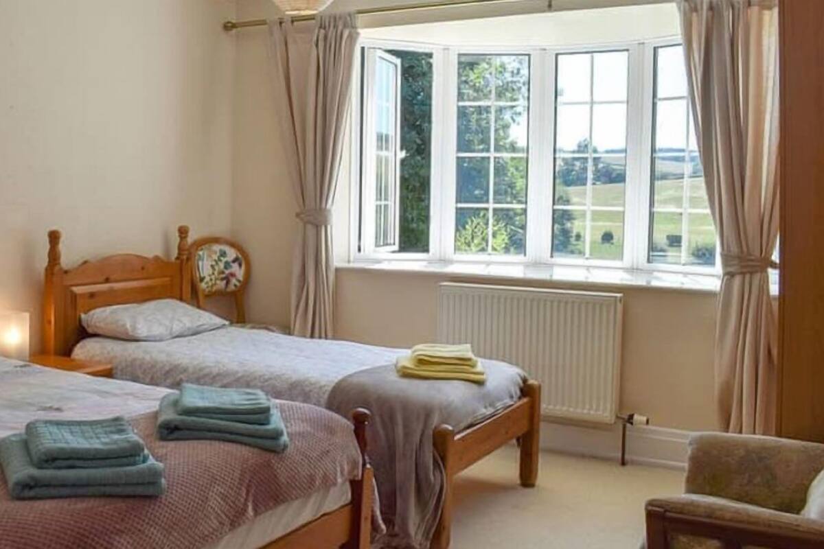 A bedroom with two beds, a window with curtains, a radiator, and a chair.