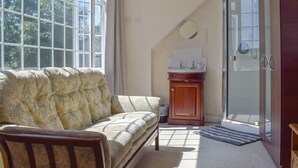 A living room with a sofa, a wooden cabinet, and a glass door leading to a bathroom. - Turpins Ride (Chalfont St Giles)
