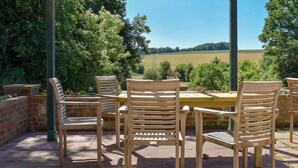 A patio with wooden chairs and a table, surrounded by brick walls and greenery. - Turpins Ride (Chalfont St Giles)