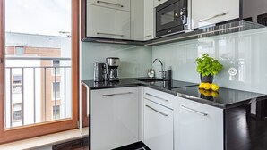 Une cuisine moderne avec des armoires blanches, un comptoir noir et une fenêtre donnant sur un immeuble.