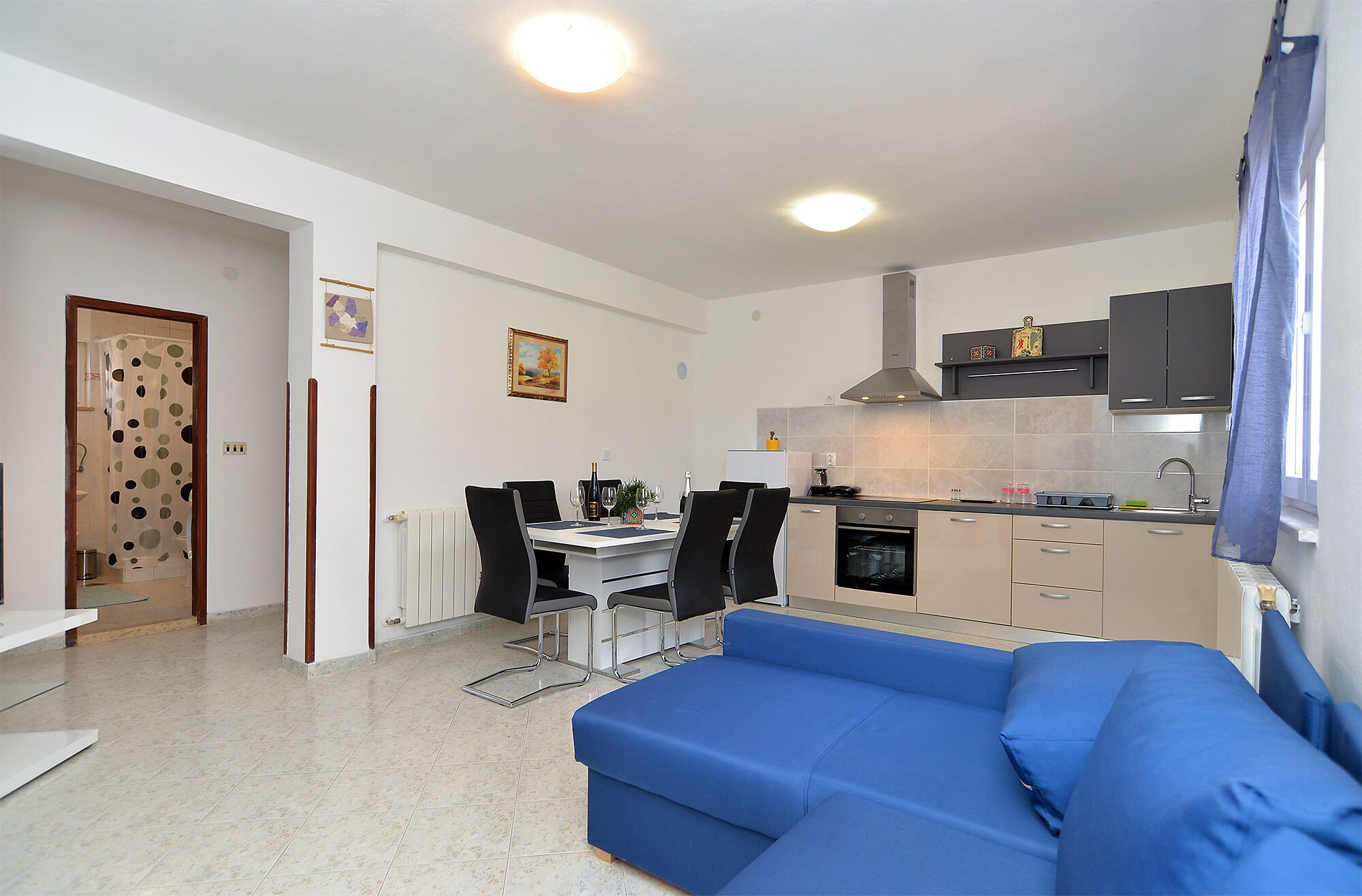 A modern kitchen with a dining area, a blue sofa, and a shower with a polka dot curtain.