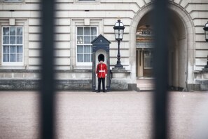 Un agent en uniforme se tient devant un bâtiment doté d’une grande entrée en arc de cercle et d’un lampadaire.