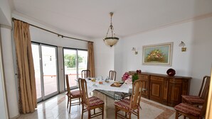 A dining area with a glass table, wooden chairs, a chandelier, and a view through the glass door. - Villa Atlantida, a charming hillside villa with a fabulous pool, great sea view. (Albufeira)