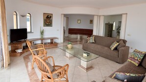 A spacious living room with a glass coffee table, wicker chairs, a brown sofa with patterned cushions, a flat-screen TV, and a dining area with a wooden table and chairs. - Villa Atlantida, a charming hillside villa with a fabulous pool, great sea view. (Albufeira)